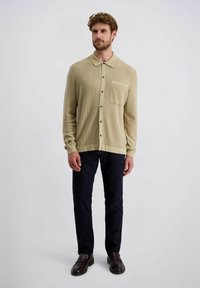 Beige Langarmhemd mit Kragen, strukturiertem Stoff, Brusttasche und Knopfverschluss, kombiniert mit dunkelblauen Hosen und dunklen Slippern.