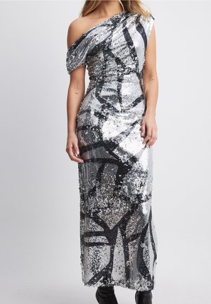 Femme portant une longue robe argentée à sequins à une épaule avec des motifs abstraits noirs, associée à des bottines noires.