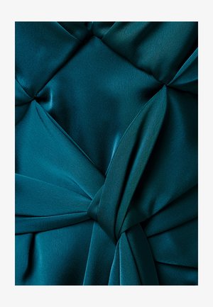 Turkooise stof met een decoratieve knoop en plooien die een gestructureerd, gelaagd patroon creëren.