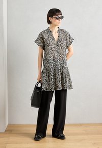 Svart og beige leopardmønstret kjole med korte ermer, lagdelt kant, sammen med brede svarte bukser, svart håndveske og solbriller.
