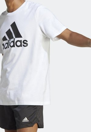 White cotton t-shirt with a black Adidas logo on the front. Short sleeves, relaxed fit. Paired with black athletic shorts featuring a small logo.