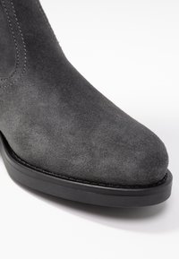Gray suede ankle boot with a rounded toe and black rubber sole, featuring subtle stitching details. Smooth texture and clean design.