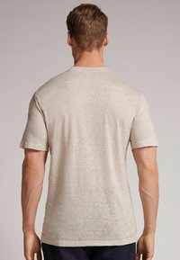 Světle béžové tričko s krátkým rukávem vyrobené z měkké, strukturované tkaniny. Má klasický kulatý výstřih a volný střih, který ukazuje hladký zadní povrch.