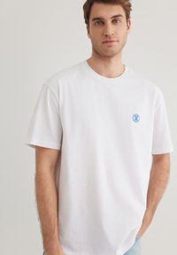 White cotton t-shirt with a round neckline and short sleeves. Features a small blue embroidered logo on the left chest.