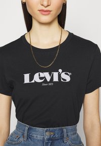 Musta puuvillapaita, jossa on suuri valkoinen "Levi's" -logo ja teksti "Since 1873", yhdistettynä korkeavyötäröisiin sinisiin farkkushortseihin.