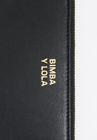 Zwart leren portemonnee met reliëf gouden tekst "BIMBA Y LOLA," een textuur oppervlakte en gouden ritsdetails.