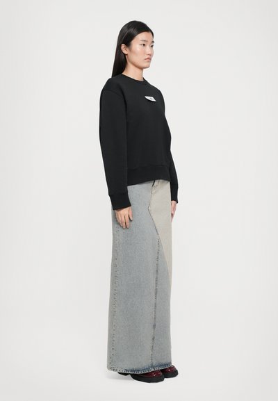 Black cotton sweatshirt with a crew neck and logo patch, paired with a long, light blue denim skirt featuring an asymmetrical design and dark accents.