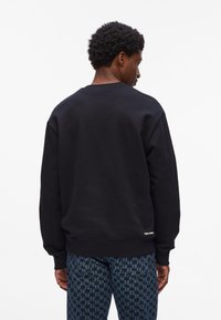 Čierna mikina s dlhými rukávmi, okrúhlym výstrihom a rebrovanými manžetami. Nosí sa s károvanými modrými džínsy s designom houndstooth.