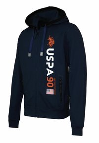Tengerészsötét kék zipzáras kapucnis pulóver fekete díszítéssel, a "USPA" és "90" felirattal fehér és narancssárga színben, cipzáras zsebekkel és amerikai zászlós öltéssel.