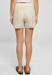 Shorts en dentelle beige avec un ourlet en forme de découpe, une taille élastique et un motif floral complexe, associés à des sandales à lanières.