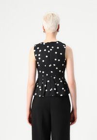 Svart peplum-top med hvite prikker, ermene er uten design, strukturert stoff, med glidelås bak. Enkle sorte bukser under.