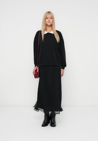 Svart oversized genser med hvit krage, parret med en plisserte svart maxiskjørt og svarte ankelstøvler. Rød crossbody-veske.