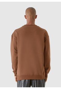 Brun sweatshirt med rundad halsringning, texturerad tyg och lång ärm. Bakifrån syns ribbade manschetter och nederkant. Slät yta.