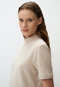 Top in misto lana beige con collo alto e maniche corte. Tessuto morbido e un leggero motivo melange, progettato per una vestibilità comoda.