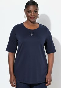 Camisa de manga corta de color azul marino con cuello redondo, que presenta un diseño geométrico en el centro. Tela suave y lisa con un ajuste relajado.