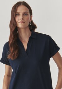 Navyblauw polo-shirt met een V-hals en opgerolde korte mouwen. Zacht materiaal en een relaxte fit, waardoor een casual silhouet ontstaat.