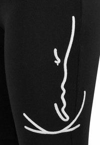 Schwarze Leggings mit einer weißen abstrakten Linienzeichnung an der Seite. Hergestellt aus weichem, dehnbarem Stoff mit einer glatten Textur.