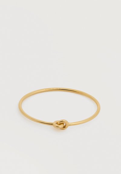 Λεπτό χρυσό βραχιόλι με μικρή διακοσμητική λεπτομέρεια κόμπου, απεικονίζεται σε απλό ανοιχτό φόντο.