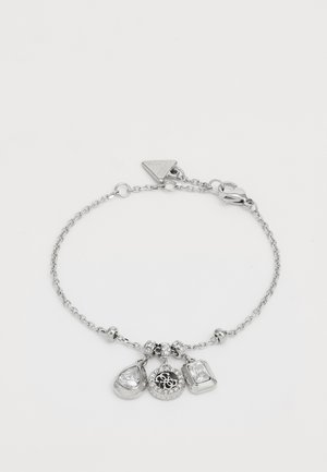 Bracelet en chaîne argentée avec trois charms : un en forme de goutte, un charm circulaire avec des embellissements, et un charm rectangulaire.