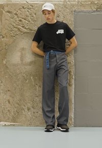 Calças largas cinzentas com cinto xadrez azul, combinadas com uma t-shirt preta e um chapéu branco de marca. Ténis pretos com detalhes brancos.