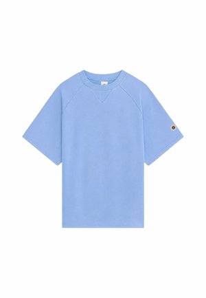 T-shirt à manches courtes bleu clair avec un petit patch circulaire sur la manche gauche et un col côtelé.