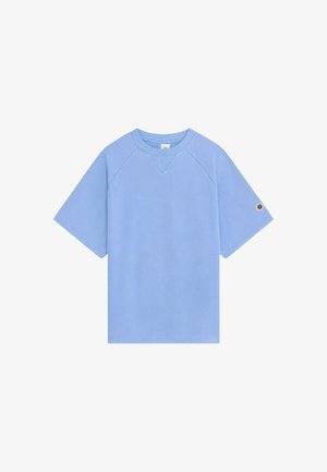 T-shirt à manches courtes bleu clair avec un petit patch circulaire sur la manche gauche et un col côtelé.