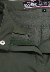 Pantaloni da esterno verdi con una texture liscia, dotati di una cintura elastica, bottone in metallo e etichetta in tessuto che indica la taglia e le istruzioni per la cura.