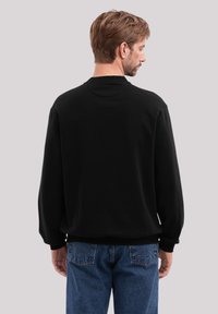Schwarzer Sweatshirt mit lockerer Passform, Rundhalsausschnitt und gerippten Bündchen. Kombination mit blauen Jeans, die an den Taschen eine auffällige Naht haben.