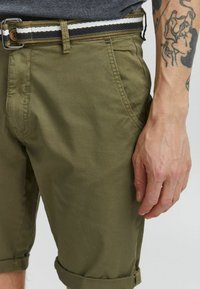 Shorts chino vert olive en coton, avec des ourlets retroussés, des poches latérales et une ceinture tissée multicolore avec une boucle en métal.