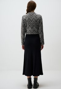 Cardigan en tricot à motif chevron gris et noir, associé à une jupe noire unie de longueur genou, porté avec des bottines noires à la cheville.