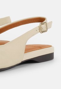 Zapato slingback de cuero beige con una pequeña hebilla dorada, plantilla color marrón claro y un bajo tacón marrón oscuro. Textura suave con detalles de diseño mínimos.