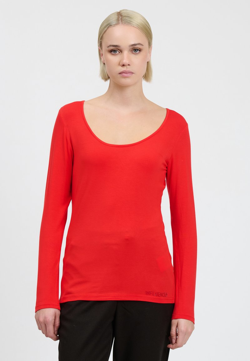 T-shirt a maniche lunghe rossa con scollo a giro, realizzata in un tessuto liscio. Presenta un piccolo dettaglio testuale "INFLUENCE" sull'orlo.