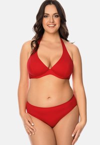 Set bikini rosso con top a triangolo e collo halter, abbinato a un fondo a vita alta, realizzati in un materiale liscio e elasticizzato.