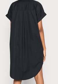 Vestito nero, morbido e ampio, con maniche corte arrotolate, dettaglio plissé sul retro e orlo curvo. Tessuto in cotone con una superficie liscia.