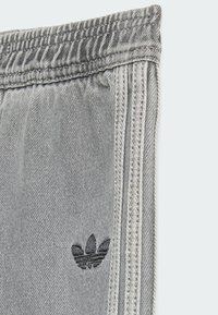Graue Jogginghosen verfügen über einen elastiche Taille, seitliche Nähte und ein kleines schwarzes gesticktes Logo. Der Stoff hat eine weiche Textur.