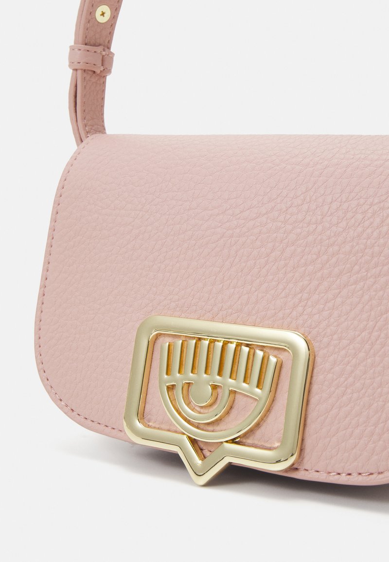 Bolso de piel rosa con un acabado texturizado, que presenta un detalle de cierre en forma de ojo en tono dorado en la parte frontal. Incluye una correa ajustable.