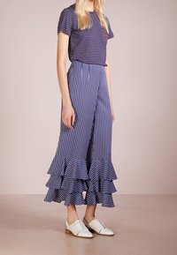 Námořnické a bílé pruhované tričko v kombinaci s odpovídajícími širokými kalhotami s volánovým lemem, doplněné bílými šněrovacími botami.