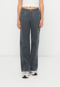 Grå vida jeans med hög midja, med sydda detaljer, framfickor och en slät yta. I kombination med ljusa sneakers.
