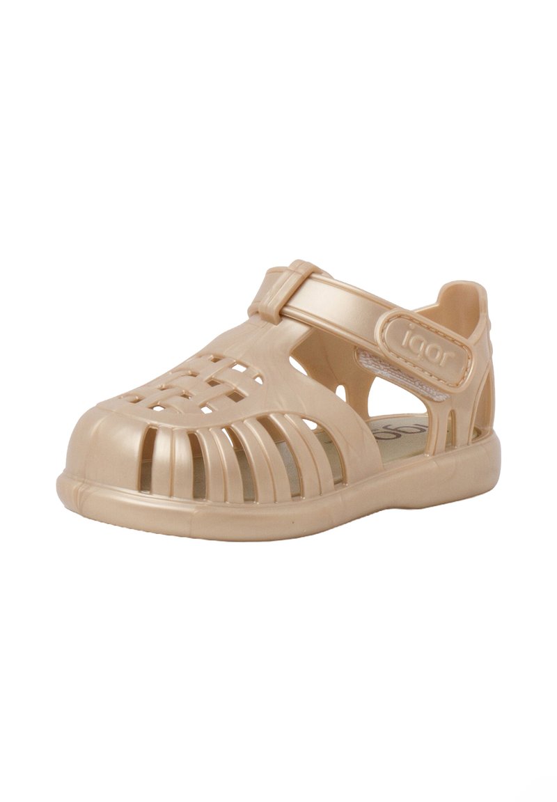 Beige plastic sandal with a closed toe, multiple cutouts for ventilation, and an adjustable strap. Smooth texture and a contoured shape.