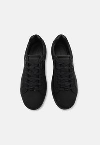 Pantofi sport negri cu o textură mată, netedă, având un design cu șireturi, un logo subtil pe limbă și o formă rotunjită a vârfului.