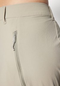 Lys beige bukser med en glat overflade, der har en sidelomme med lynlås og en skræddersyet talje. Minimalistisk design med fine stikninger.