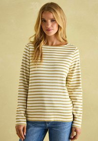 Langärmliges gestreiftes Oberteil in Weiß mit goldenen horizontalen Streifen, Rundhalsausschnitt und weichem Material, kombiniert mit blauen Jeans.