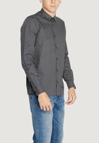 Camicia a maniche lunghe nera e bianca a fantasia con colletto a punta, abbinata a jeans azzurri chiari, realizzati in tessuto testurizzato e dal taglio slim.