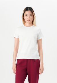 T-shirt bianca in cotone con maniche corte, scollatura rotonda e taglio dritto, indossata con pantaloni sportivi bordeaux caratterizzati da un accento stampato.