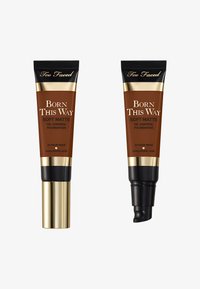 Deux tubes de fond de teint dans des teintes marron foncé. Chacun a un capuchon noir avec des accents dorés. Les étiquettes indiquent "Fond de Teint Matifié Contrôle de l'Huile Born This Way."