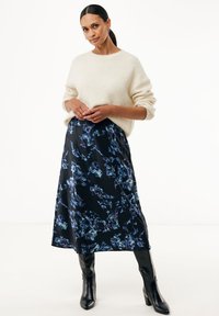 Jersey de crema con hombros caídos, combinado con una falda midi negra con flores en tonos azules. Botas negras hasta la rodilla completan el look.