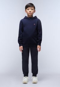 Marineblauwe katoenen hoodie met geribde manchetten, gecombineerd met bijpassende joggers. Textuurstof en een klein logo-detail op de borst. Witte sneakers.