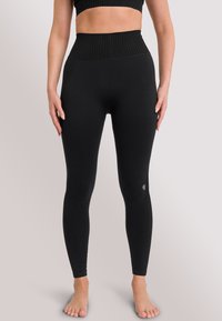 Schwarze nahtlose Leggings mit einem hohen gerippten Bund und strukturiertem Muster. Mit einem Logo-Detail am Unterschenkel. Dehnbare Stoffqualität.