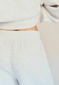 Svetlo šedá, mäkká látková mikina s kratším strihom a elastickým pásom. Zodpovedajúce svetlo šedé teplákové nohavice s voľným strihom.