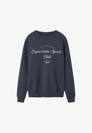 Navy zils džemperis ar baltu tekstu, kas lasa "Jāšanas Sporta Klubs", un mazāku tekstu, kas atsaucas uz sacīkstēm, jāšanu, polo un Romu.